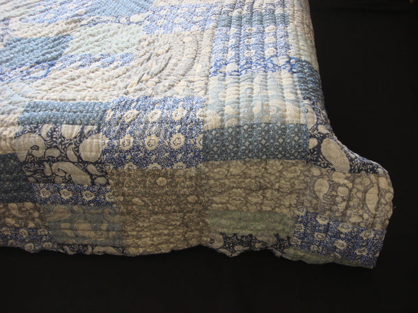 Handmade, patchwork cotton quilt in block printed blocks scattered in shades of grey and blue.