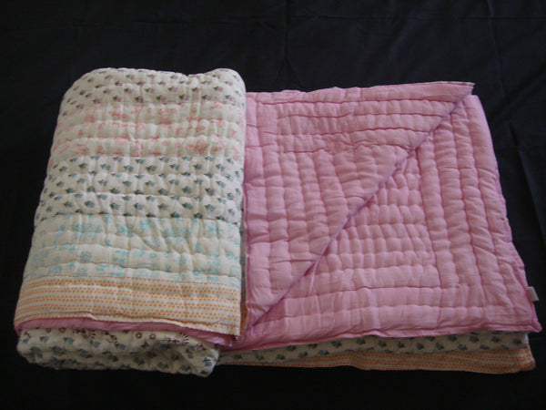 Handmade, patchwork cotton quilt in small block prints spreads in soft, pastel colors.