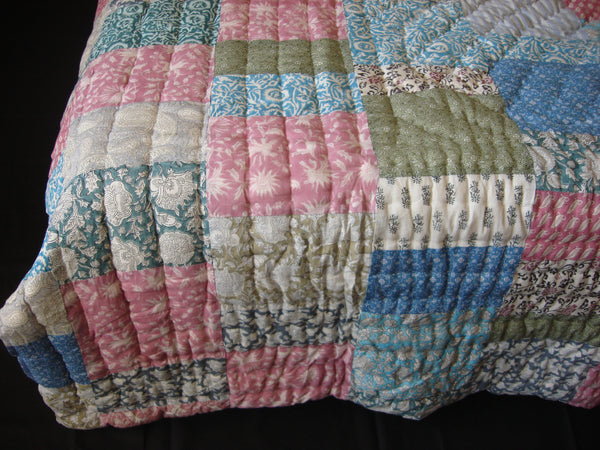 Handmade, patchwork cotton quilt in prints in shades of pink and blue
